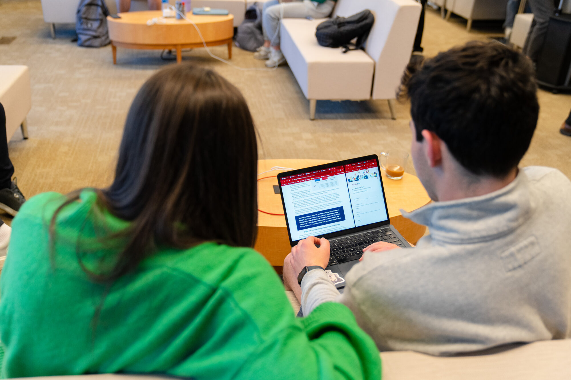 Two students working on a couch using a laptop to work on a project.